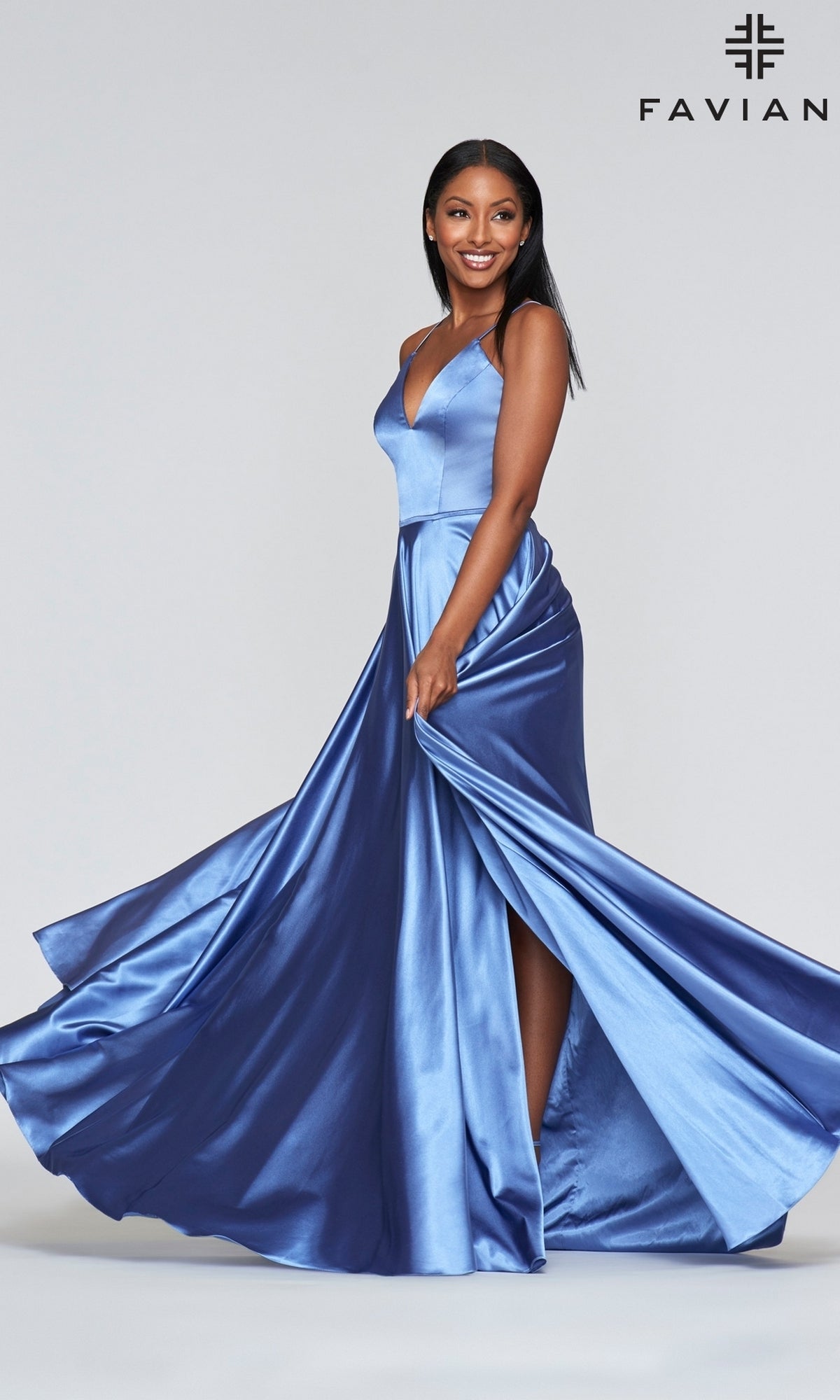A woman smiles in a sleeveless blue Long Faviana Prom Dress with Back Cut Out, featuring a high slit, posing against a plain light background. The Faviana logo is visible in the top right corner.